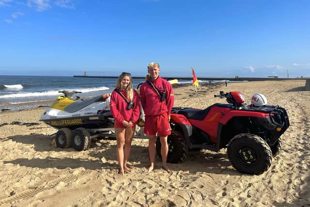 RNLI lifeguards Abby Cass (left) and Chris Trotter (right) in front of an RNLI rescue watercraft. Photo credit: RNLI. 