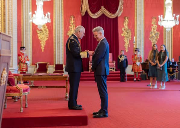 Andrew Dunn MBE receives his award from Charles III, while his daughters Theresa and Rachel look on.