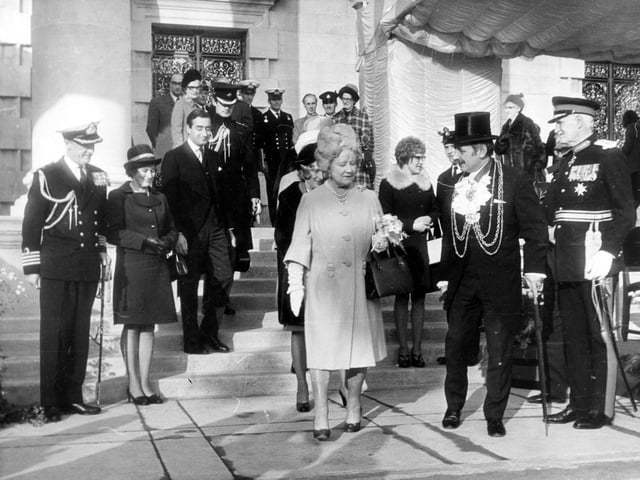 On the steps of the Civic Hall, on the left, is Captain A.D. Cassidy, who commanded the Ark Royal. To the right of the Queen Mother is the Lord Mayor of Leeds, Alderman Kenneth Travis Davison, wearing his chain of office.
