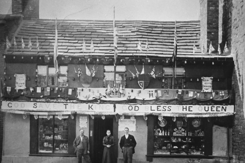 A small group outside Brown & Polson's sweet shop and tobacconist on Rothwell's Commercial Street in 1902. The building is decorated with flags and bunting to celebrate the coronation of Edward VII.