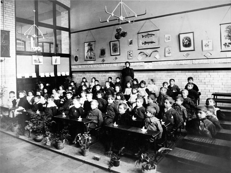 Class of infant children having a lesson in paper folding. Each child has a folded paper boat on the desk.
