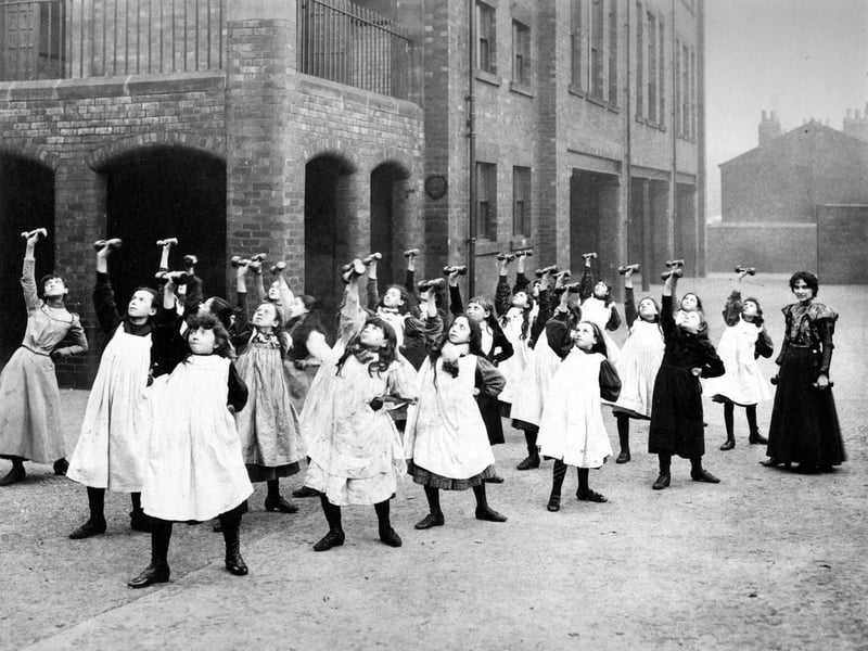 Class of girls having a drill lesson in the playground at Darley Street School. Each girl has a weight in each hand, rhythmic movements are made on command of the teacher.