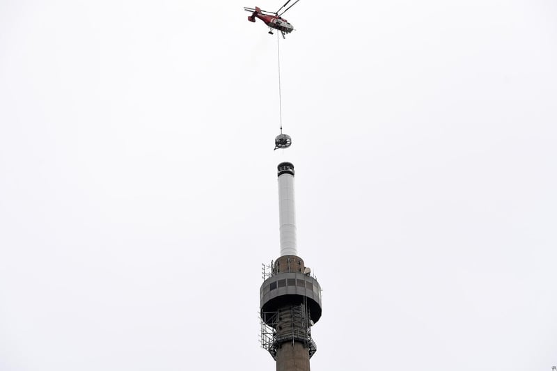 The helicopter lowers the part onto the top of the tower