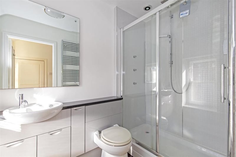 Double walk-in shower area/ mains shower, low-level WC and wash hand basin set within vanity cupboards. Chrome, heated towel rail.