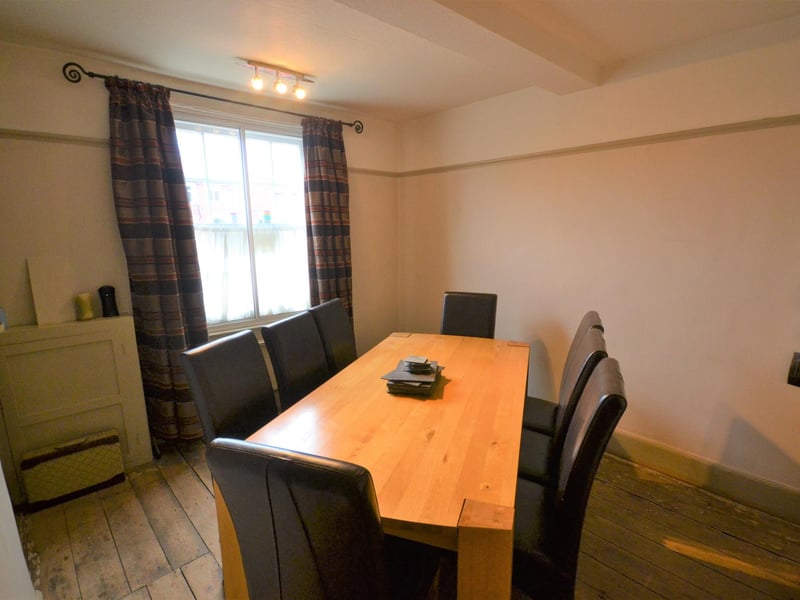 A front-facing room used as a formal dining room, having a fitted cupboard with bookcase and stripped wooden flooring.