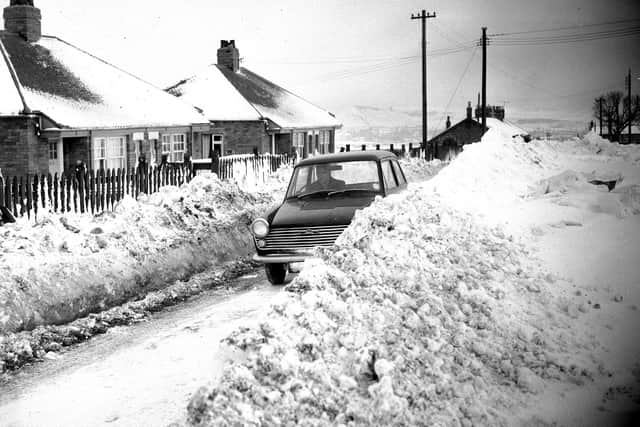 A motorist drives along the cleared road at High Moorsley, where pensioners' homes (left) were isolated by a blizzard in early January 1963.