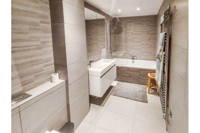 The second bathroom has a bath with overhead shower, a large sink and towel rail.