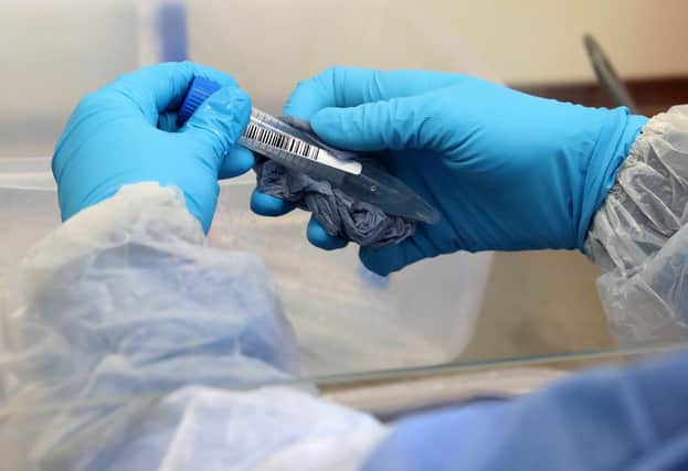 A laboratory technician wearing full PPE (personal protective equipment) cleans a test tube containing a live sample taken from people tested for the novel coronavirus. (Photo by ANDREW MILLIGAN/POOL/AFP via Getty Images)