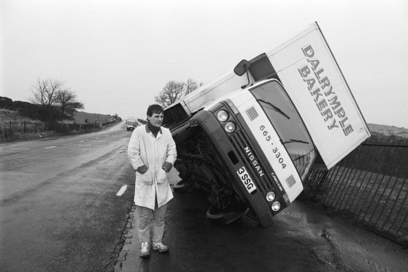 Driver Gregor Maclean stands beside his Dalrymple Bakery van, blown over in Braid Hills Road Edinburgh during the gales in December 1986.