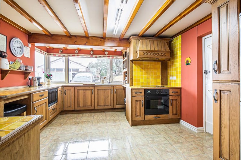 The kitchen features a range of units, integrated appliances and timber ceiling beams.