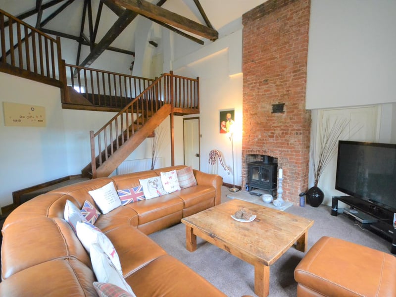 Open-plan, double-height, vaulted ceiling sitting room with exposed oak trusses to the ceiling and a wonderful and an exposed brick fireplace continuing to the ceiling.