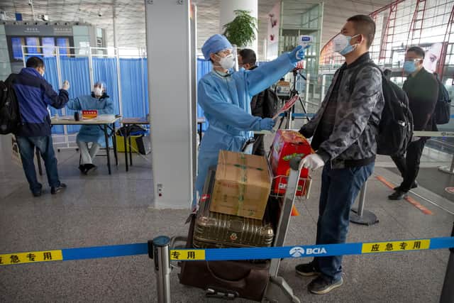 A worker in a protective suit takes the temperature of a traveler at Beijing Capital International Airport in Beijing, Friday, March 6. AP Photo/Mark Schiefelbein.