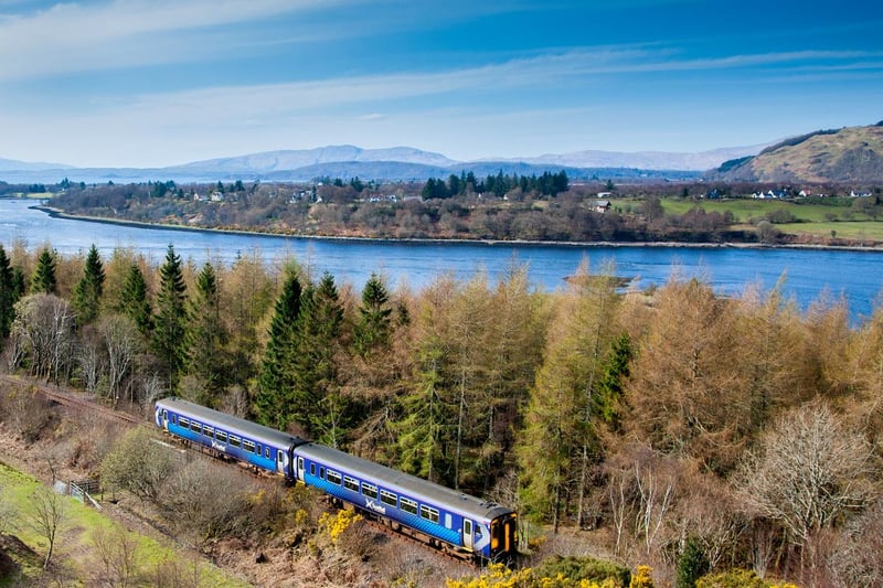 A train approaching Connel on the West Highland Line with Loch Etive with Connel Bridge in the distance.