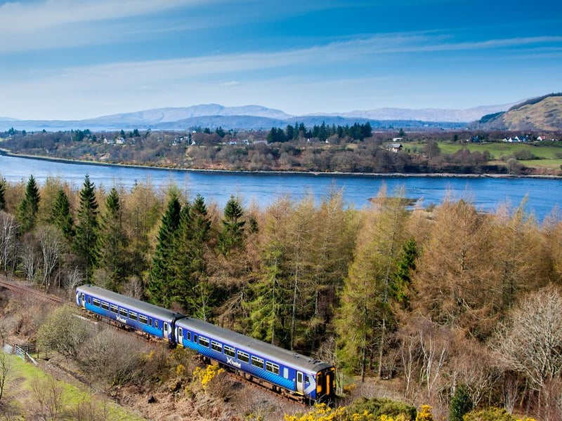A train approaching Connel on the West Highland Line with Loch Etive with Connel Bridge in the distance.
