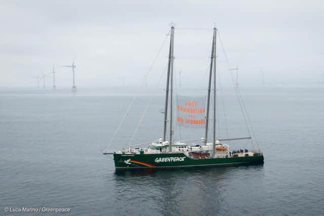 MY Rainbow Warrior with banner reading "Just Transition for Oil Workers" sails along an offshore wind farm.
