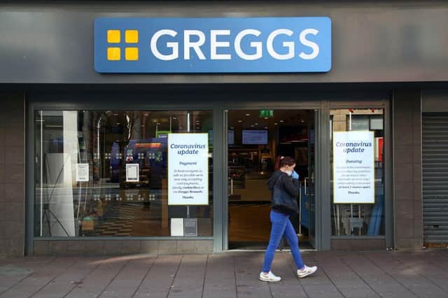An woman wearing a face mask as a precautionary measure against covid-19, walks past a Greggs bakers store.