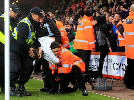A Newcastle United fan is restrained by stewards and police at Bournemouth on Saturday. Five men have been charged with entering the playing area during a football match.