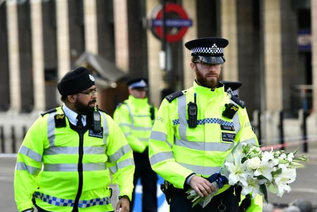 A police officer carries flowers on Westminster Bridge near to the Houses of Parliament in London, following an attack in which three people were killed when a knife-wielding attacker, named as Khalid Masood, ploughed a car through pedestrians on the bridge, before storming the Parliamentary estate, where he was shot dead