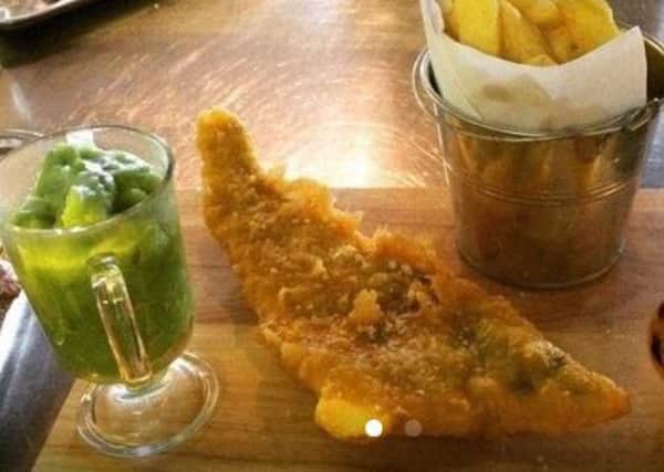 Fish and chips served on a chopping board and peas in a latte mug